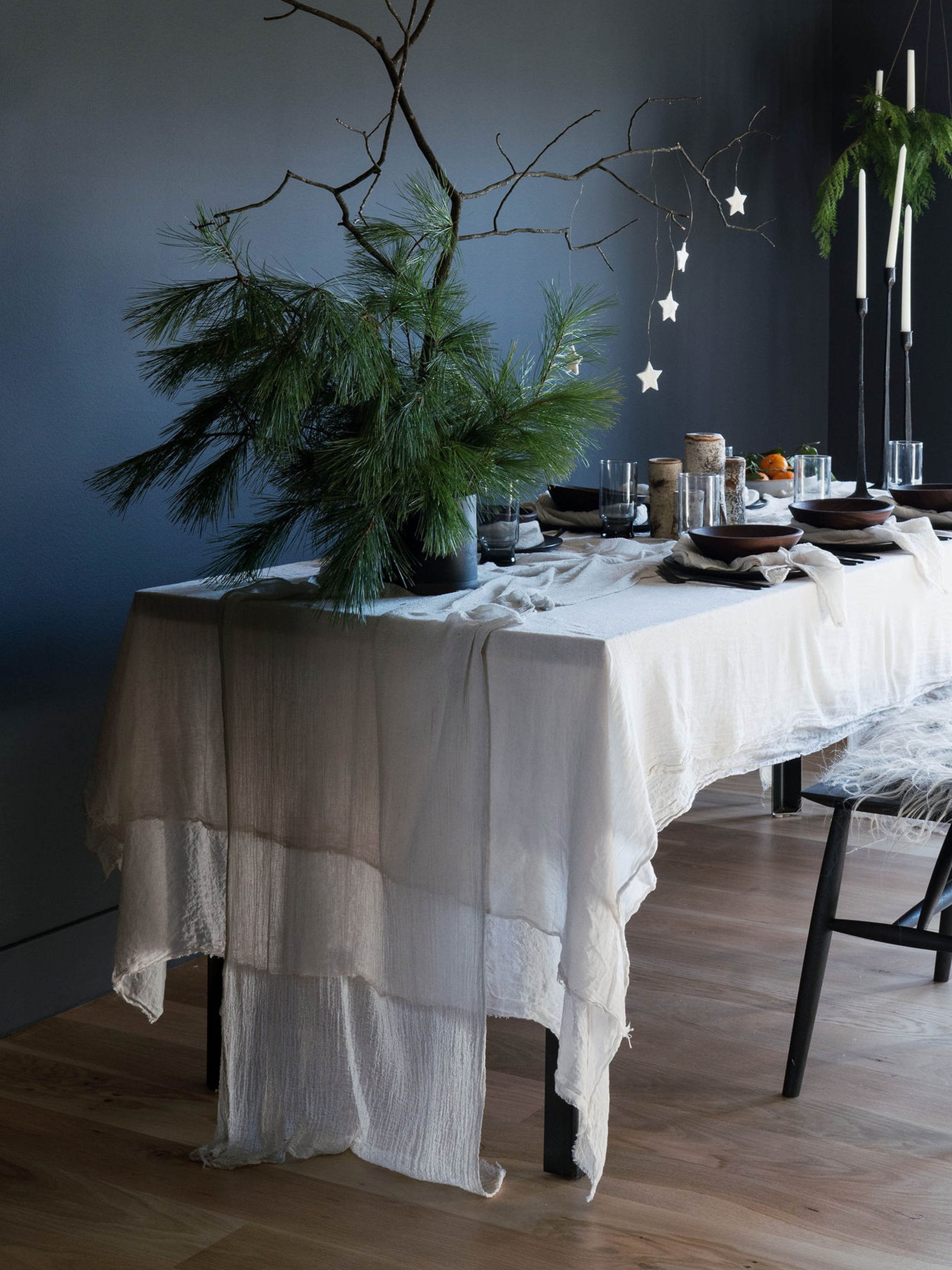 An elegantly set Nordic winter table featuring antique white, plant-dyed, handloomed cotton table runner, showcasing a wabi-sabi, organic design that highlights the heirloom quality of the table linens. Perfect for anyone seeking to create a serene and sophisticated winter tablescape.