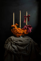 artful floral display with marigold flowers and red ribbon bows stacked on candles. Creative floral centerpiece